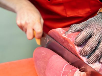 Woman cutting fresh meat in a butcher shop with metal safety mesh glove