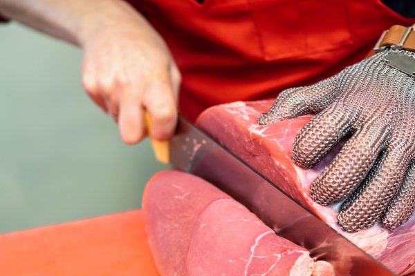 Woman cutting fresh meat in a butcher shop with metal safety mesh glove